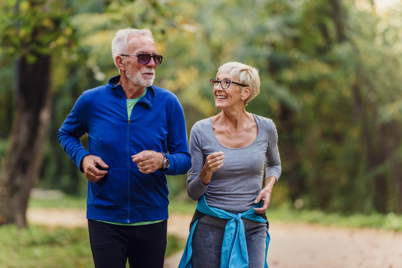 Cheerful active senior couple jogging in the park. Exercise toge